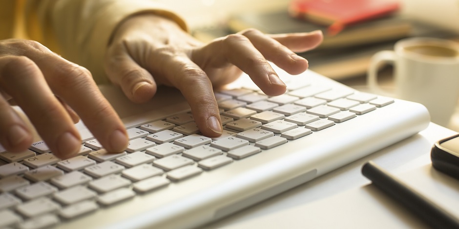 Women's fingers typing on laptop keyboard close-up.